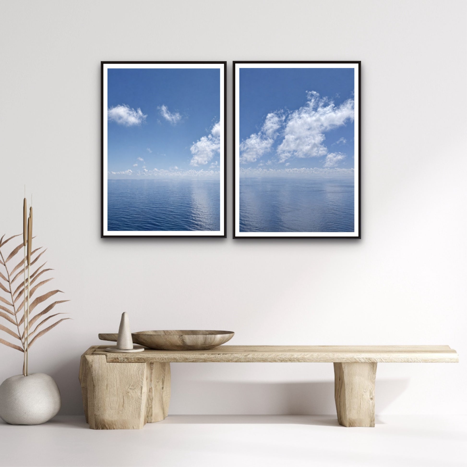 Two framed prints of a blue sky with clouds hanging on a wall above a wooden bench.