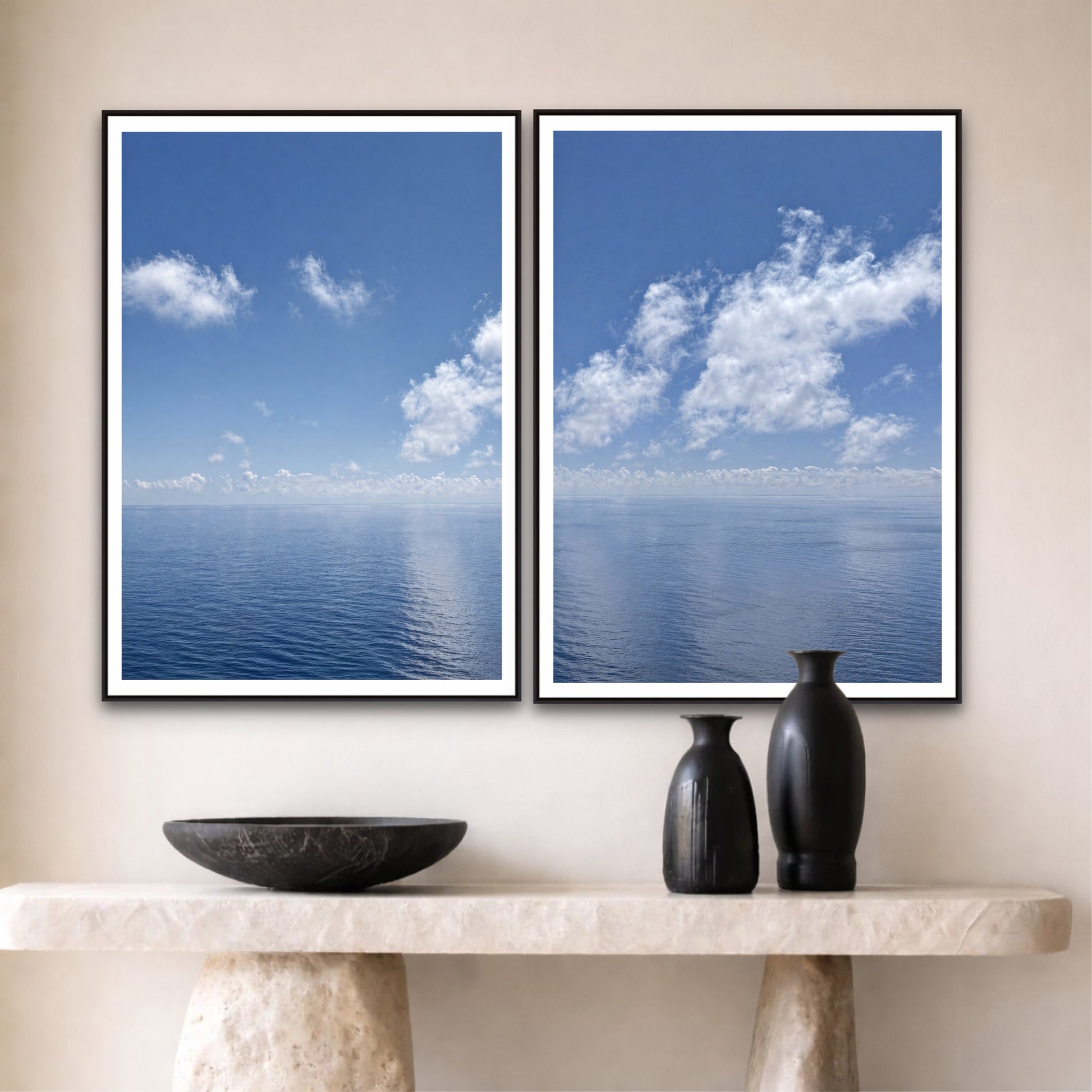 Two framed pictures of a blue sky with clouds on a wall above a marble console table with decorative items.