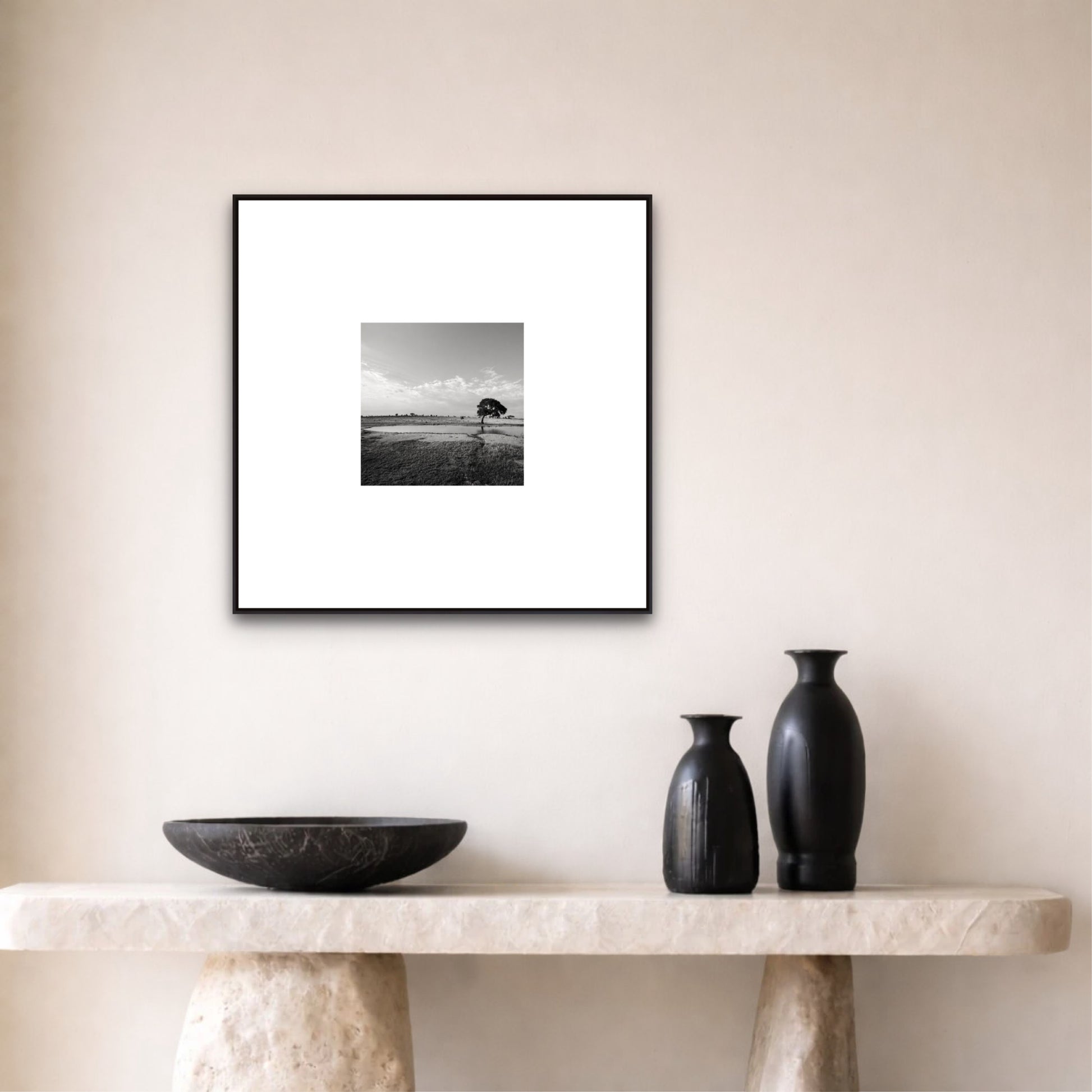 Framed black and white landscape print on a wall above a marble console table with decorative vases.