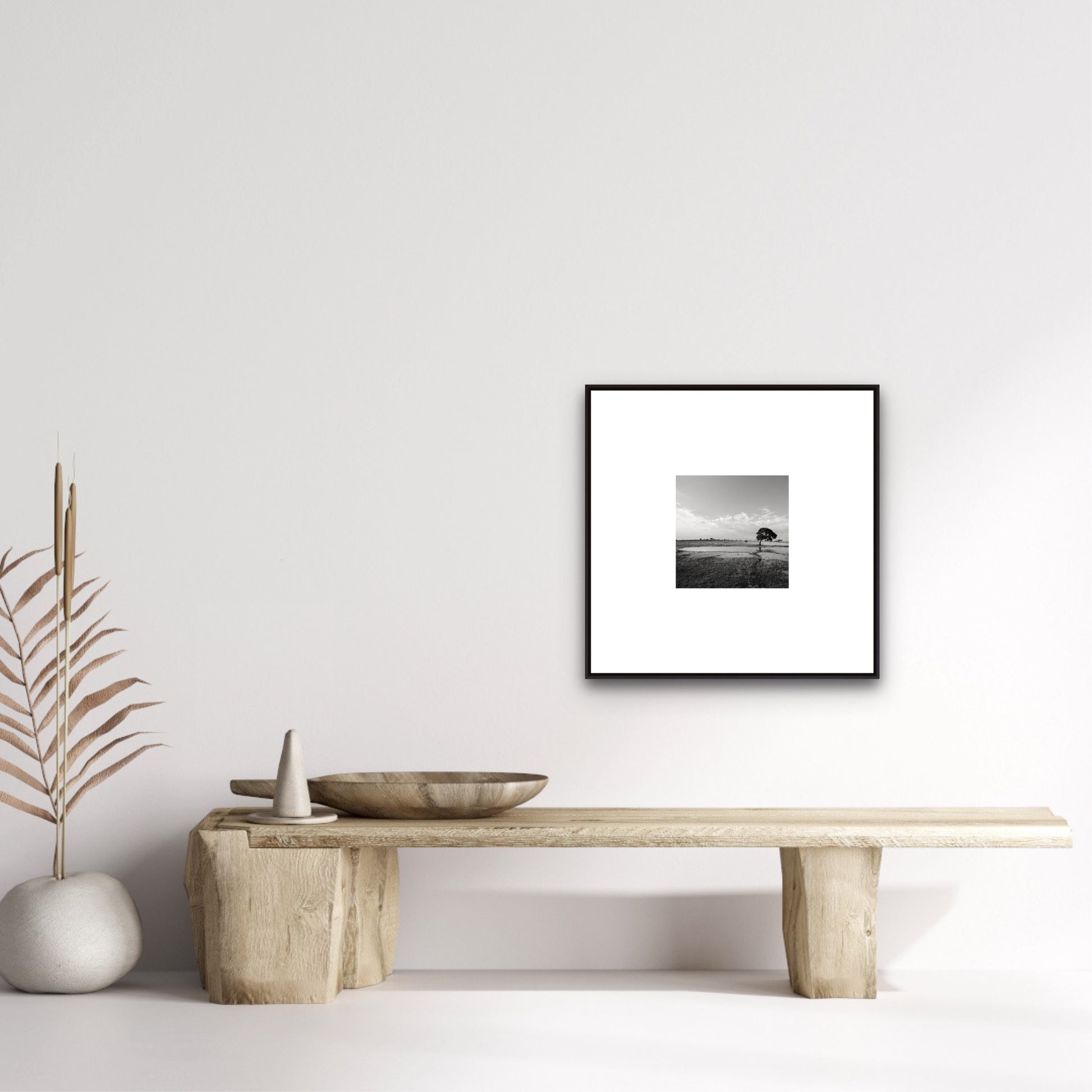 Framed black and white artwork on a wall above a wooden table with decorative items.